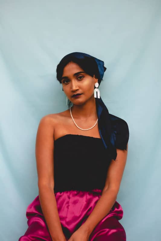 Photo of Anjalica Solomon in front of a light blue background, looking softly in the distance